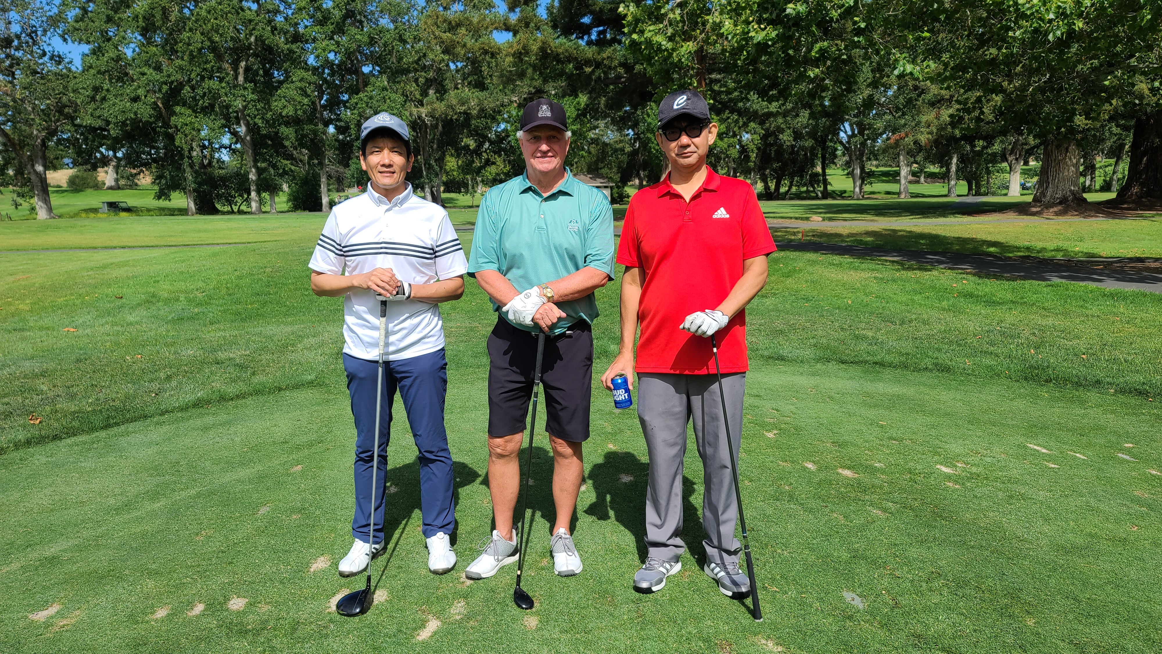 Three men wearing baseball caps standing on grass holding golf clubs.