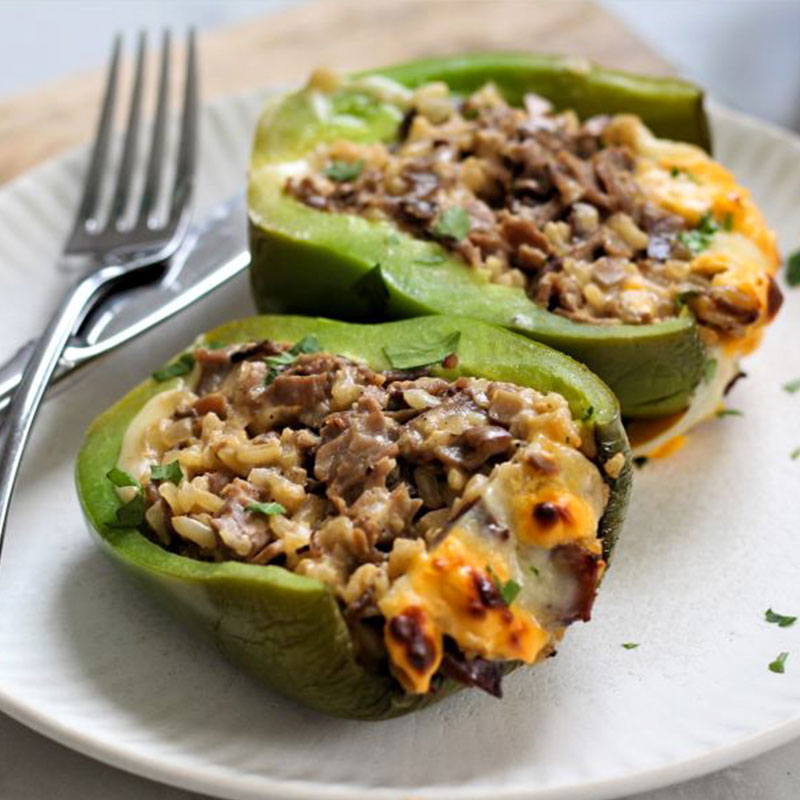 Two open faced Philly Cheesesteak Stuffed Peppers on a white plate.