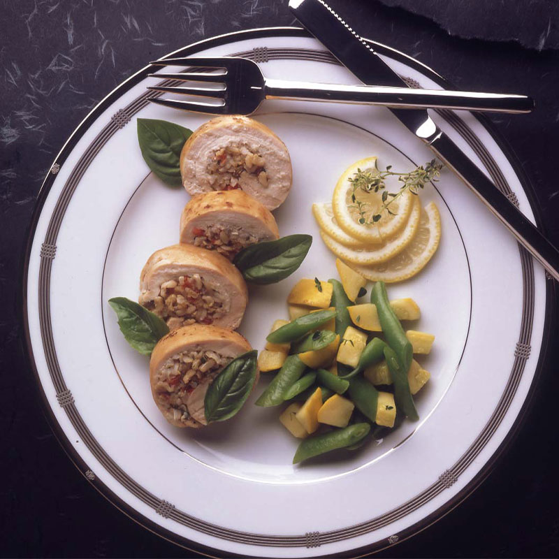 Overhead image of 4 pieces of stuffed chicken breast with lemon slices and green beans to the side.