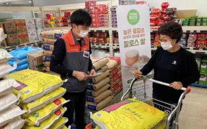 Korea promotion shows two people, both wearing masks, the man is holding papers and the woman is pushing a grocery cart filled with bags of rice