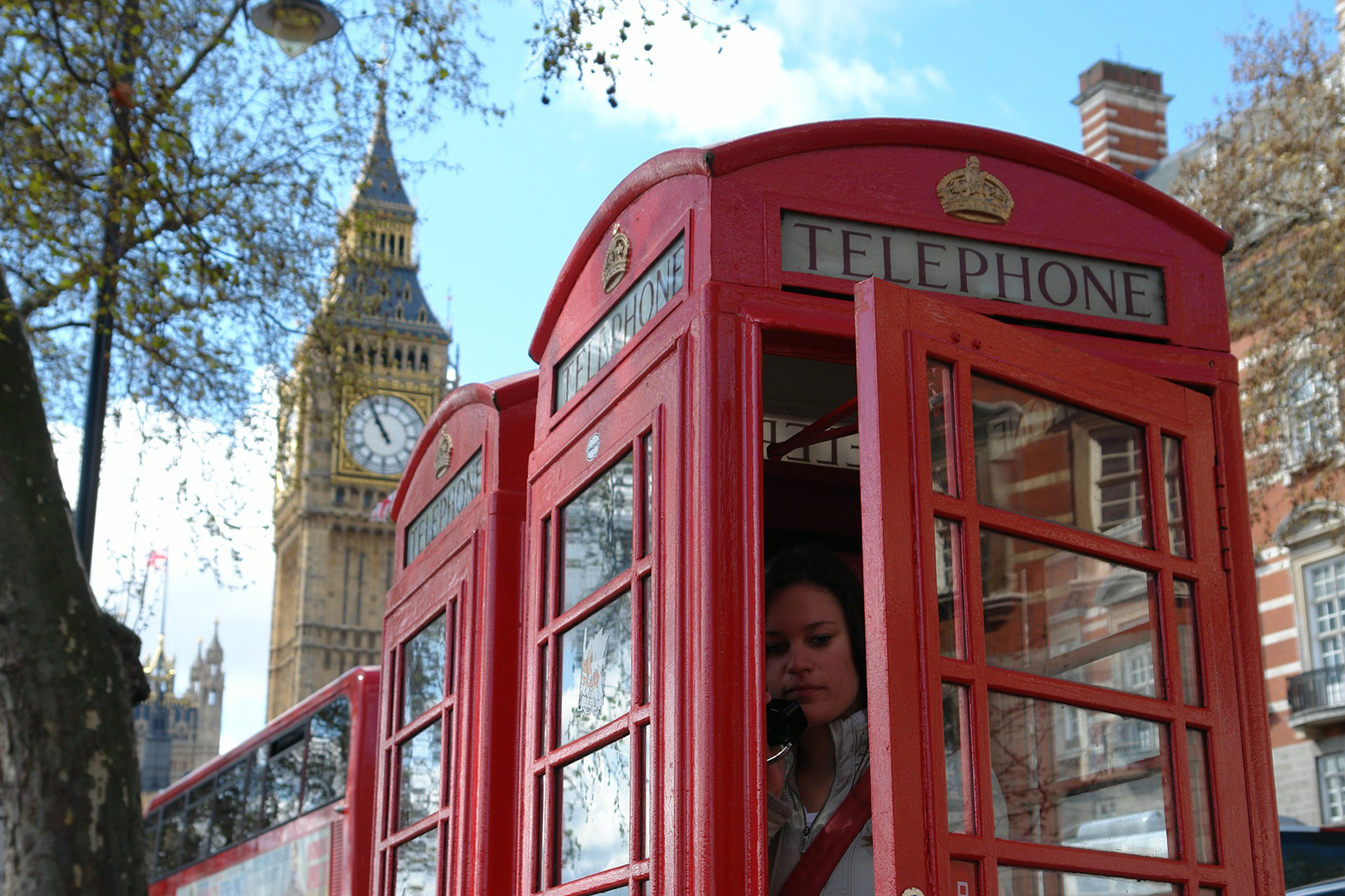 Woman on the phone inside a red UK telephone box, Big Ben in background