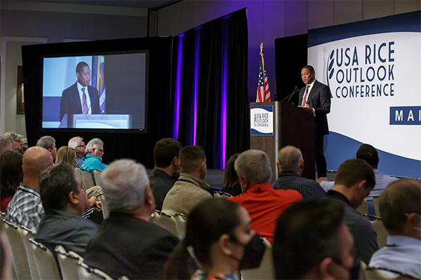 Man at a podium speaking to a crowd of conference attendees.