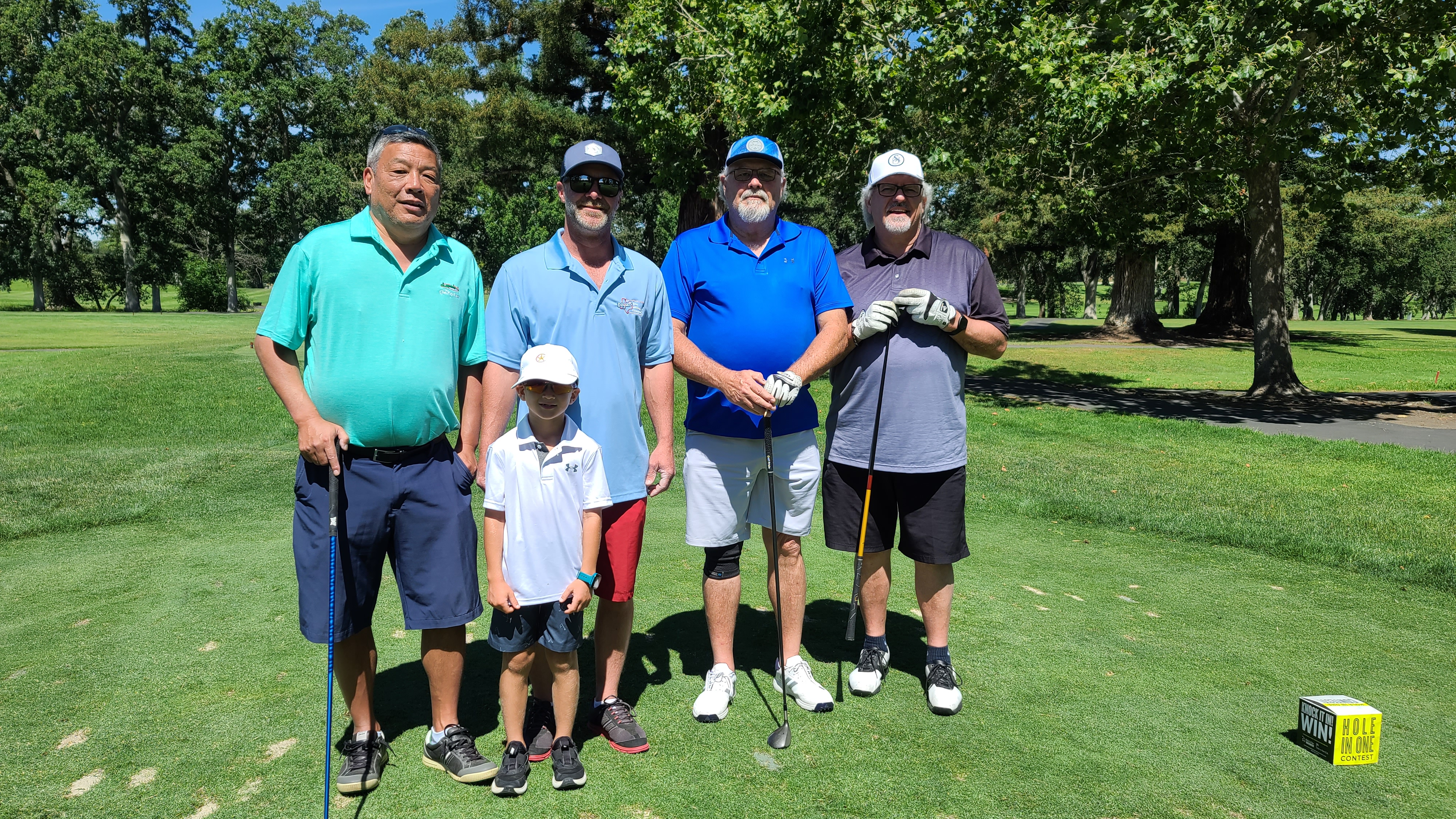 Four men holding golf clubs at a golf course.