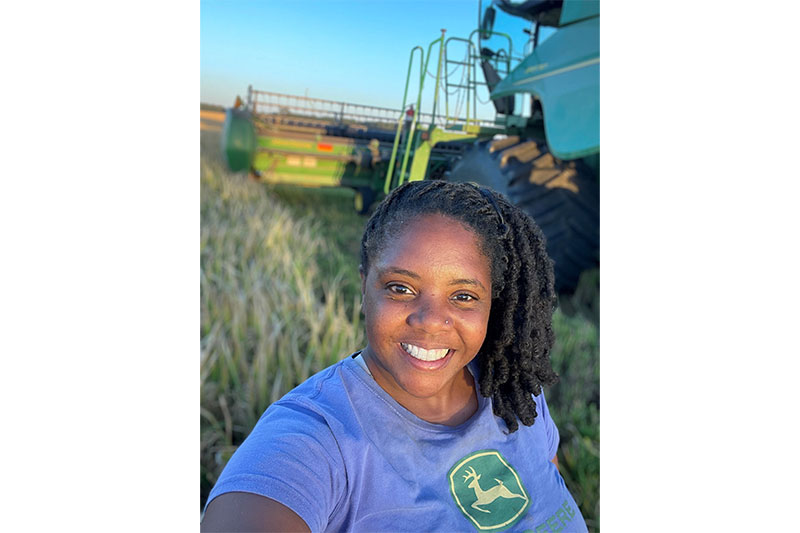 Woman smiling in front of a combine in a rice field.