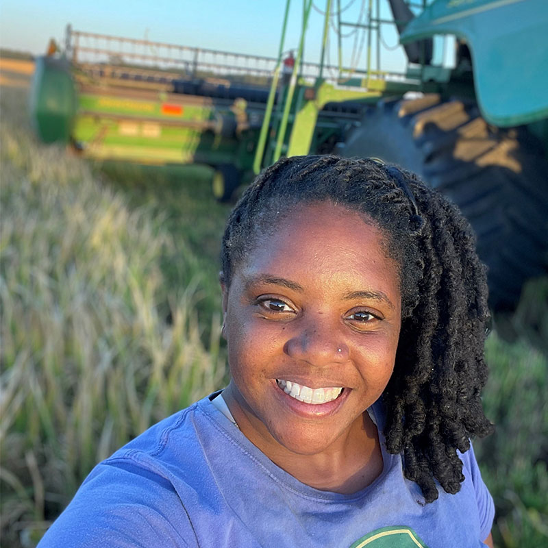 Woman smiling in front of a combine in a rice field.