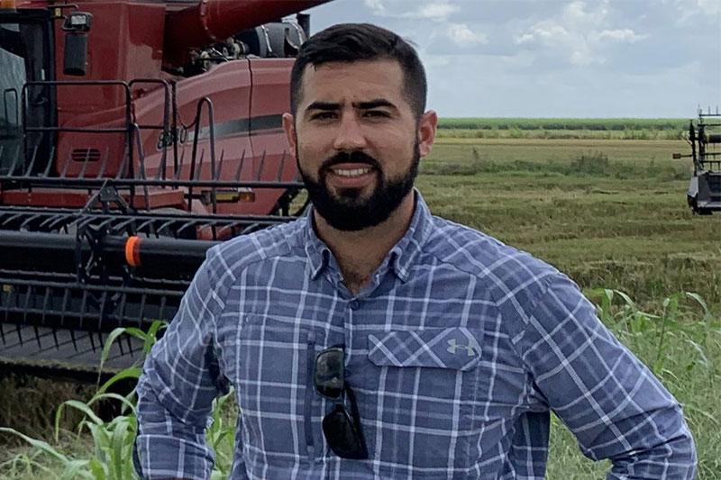 Man standing in front of a combine in a rice field.