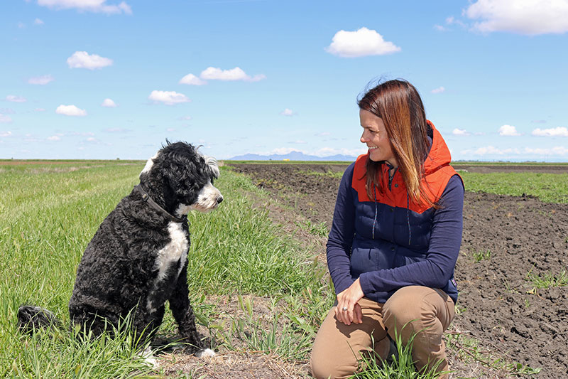 Kim Gallagher with her dog Comet in a field with blue sky.