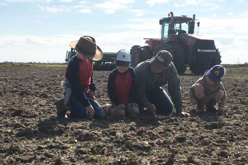 Paul Johnson examining soil in a field with his children.