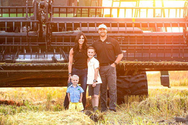 sam-schneider-wide A man, woman, and two boys standing in a rice field in front of a combine at sunset.