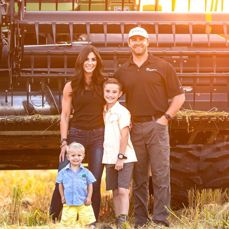 A man, woman, and two boys standing in a rice field in front of a combine at sunset.