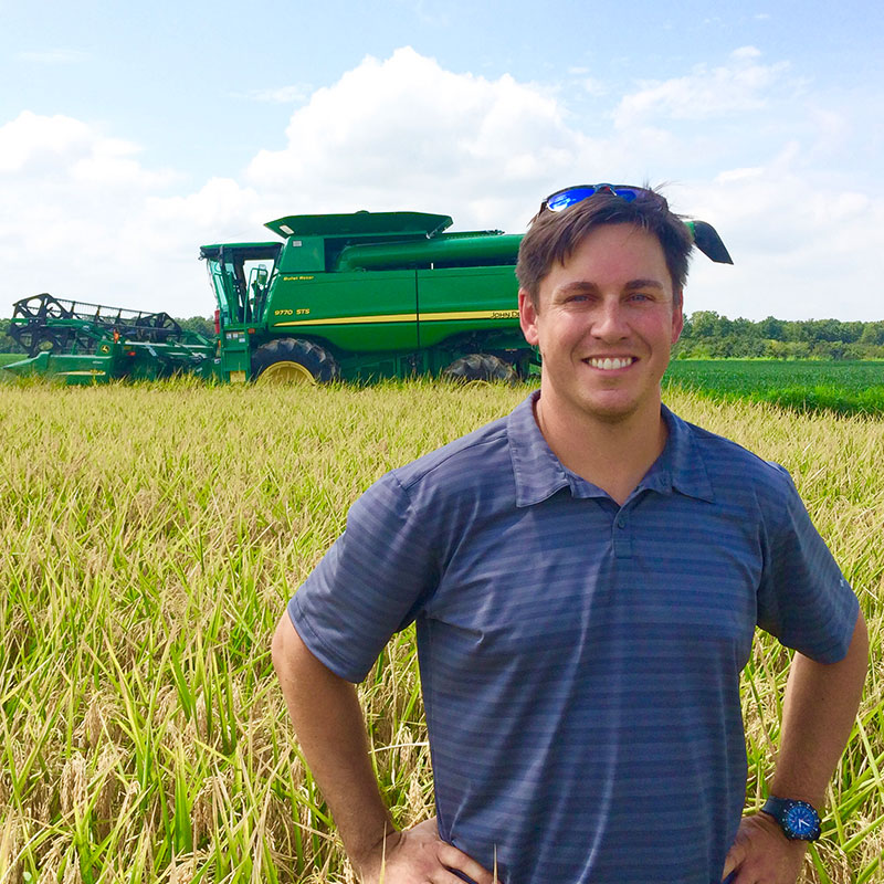 Rice farmer, Sidney Robnett, standing in a rice field with combine in the background.