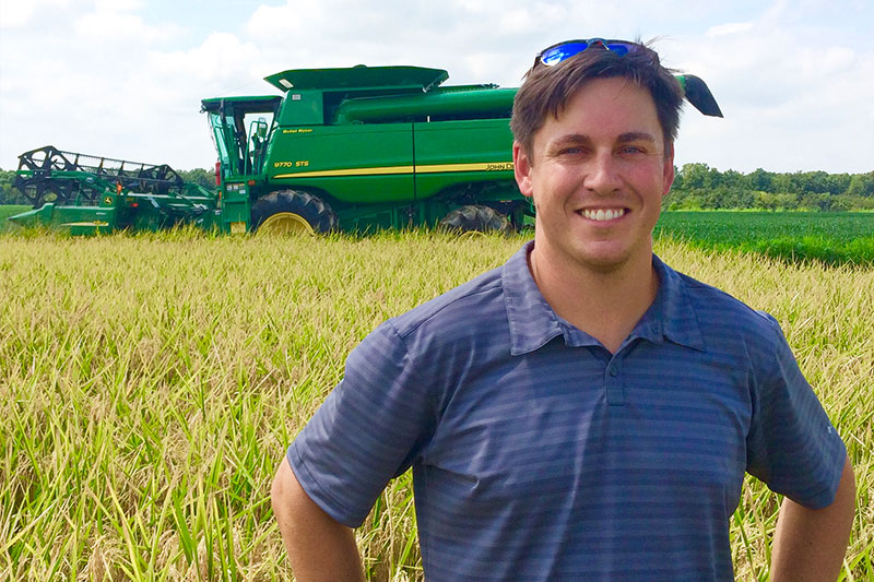 Rice farmer, Sidney Robnett, standing in a rice field with combine in the background.