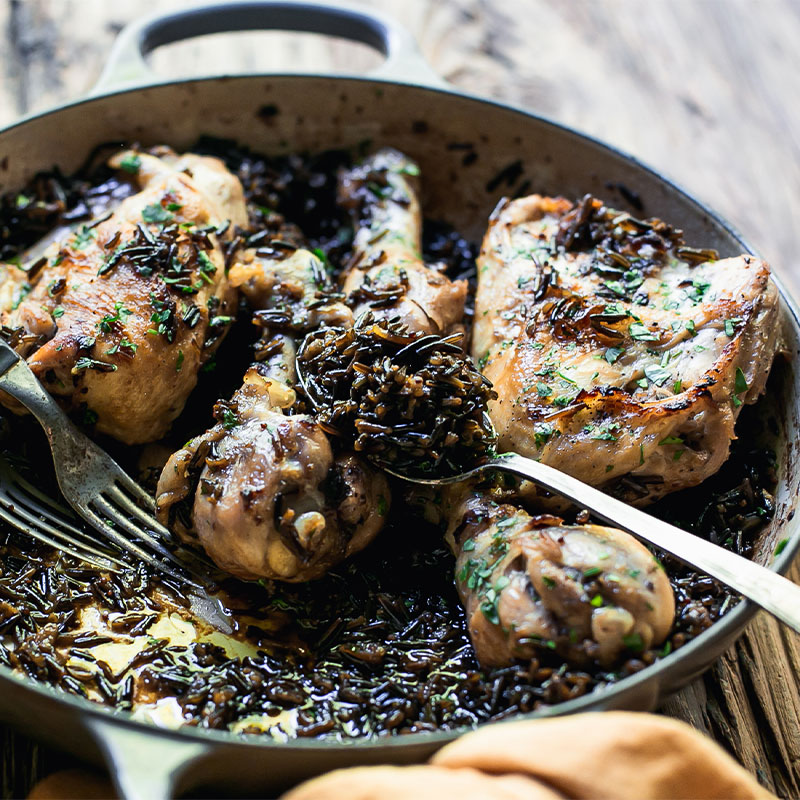 Side shot of Cider Braised Chicken with Wild Rice in a pan with a spoon on the side filled with a spoonful of Wild Rice.