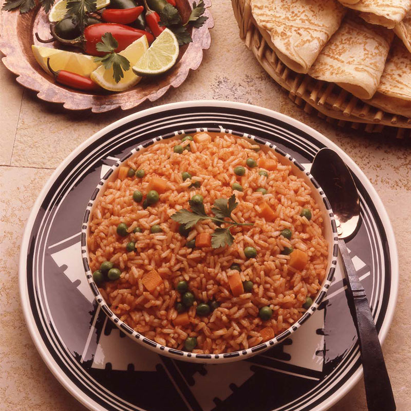 Overhead view of a bowl of Arroz a la Mexicana with tortillas and sliced limes.