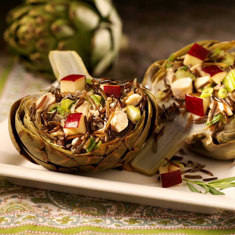 Side view of artichokes stuffed with chicken and wild rice on a white plate.