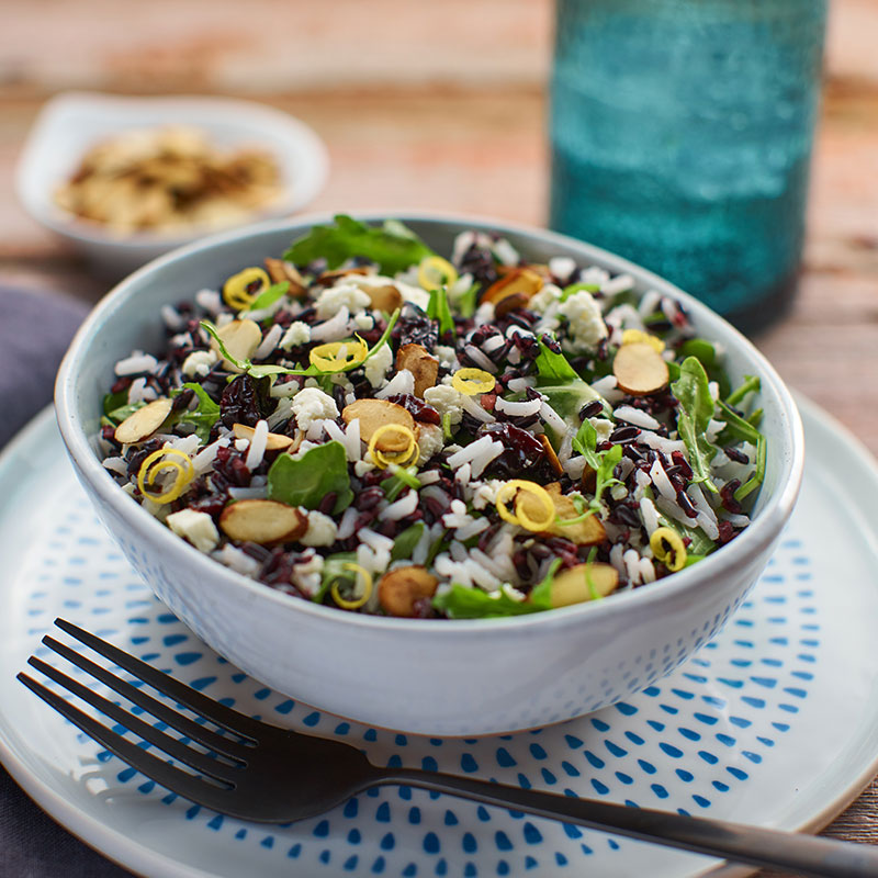 Side view of arugula and rice salad in a blue bowl.