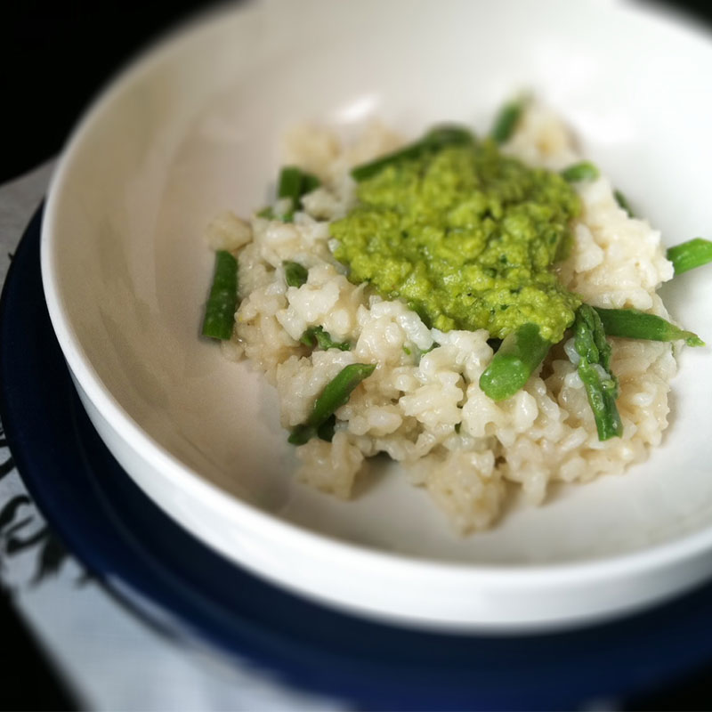 Close up of asparagus risotto in a white bowl topped with spring pea pesto.