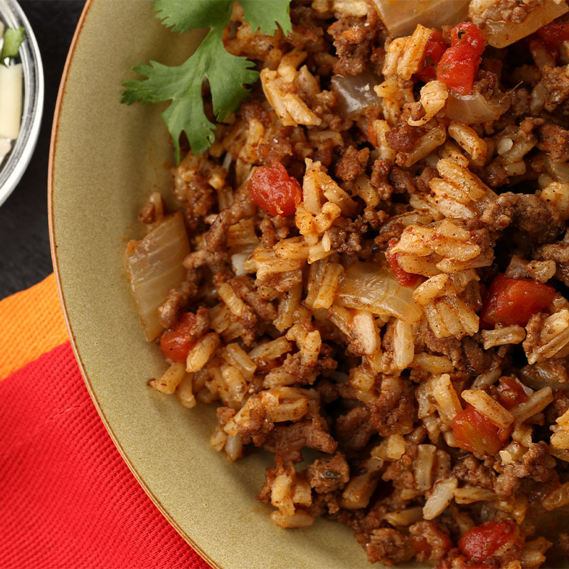 Zoomed in view of a plate full of a white rice and ground beef mixture with onions and tomatoes.