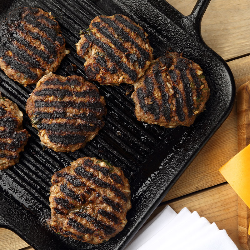 Overhead image of a skillet with 6 grilled hamburger patties.