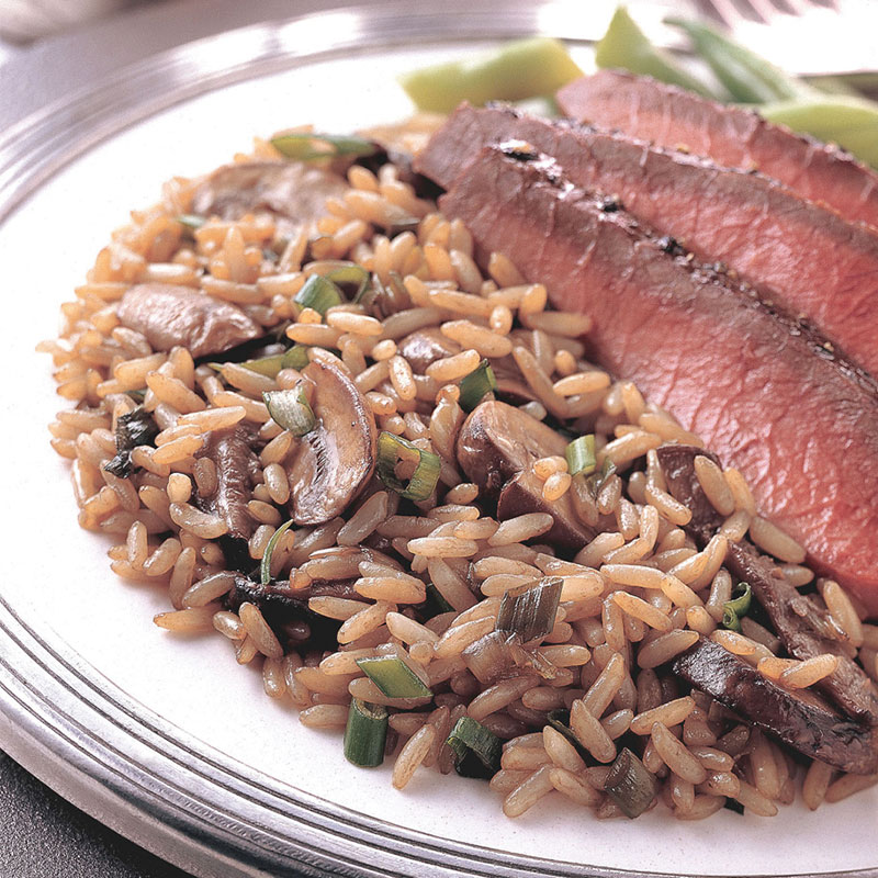 Side view of beef simmered rice and mushrooms on a white plate with sliced beef and green beans.