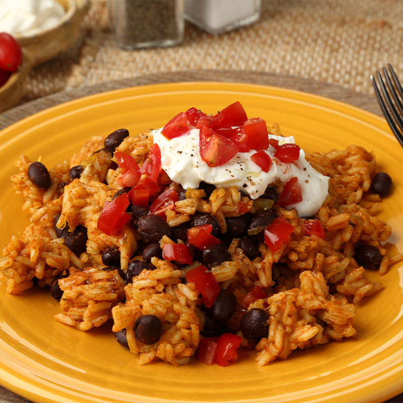 Hearty serving of Black Bean & Green Chili Rice topped with sour cream and cut tomatoes. 