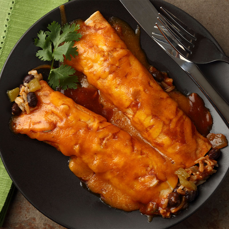 Overhead image of two enchiladas covered in sauce on a black plate.