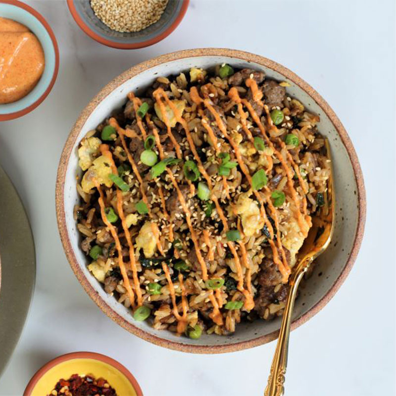 Overhead shot of a bowl of Breakfast Fried Rice topped with a drizzle of sauce.