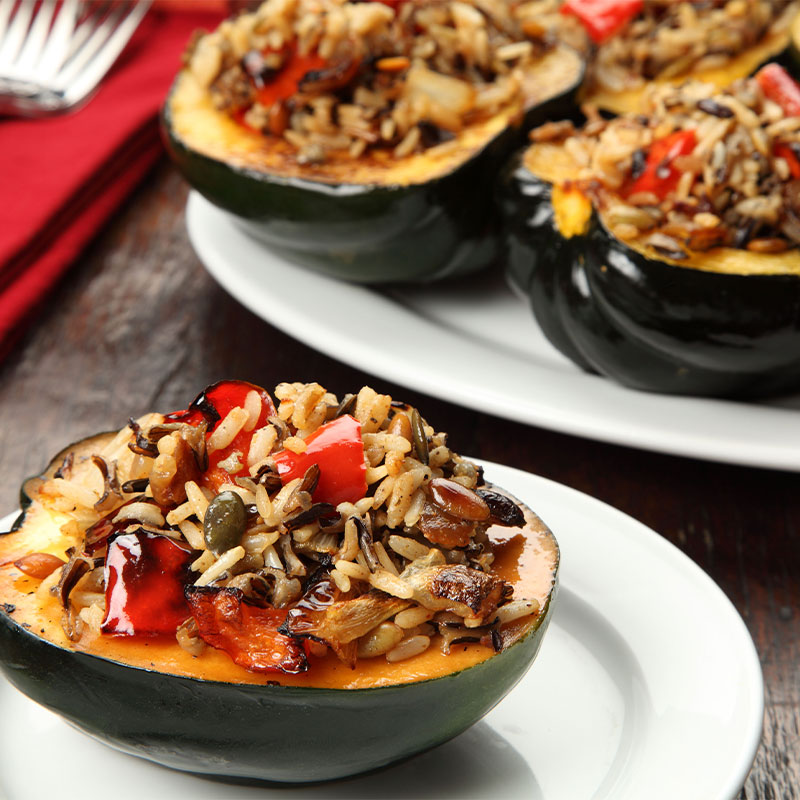 Brown and Wild Rice Stuffed Squash Side profile of one Brown and Wild Rice Stuffed Squash on a white plate with a second plate of Brown and Wild Rice Stuffed Squashes behind it.