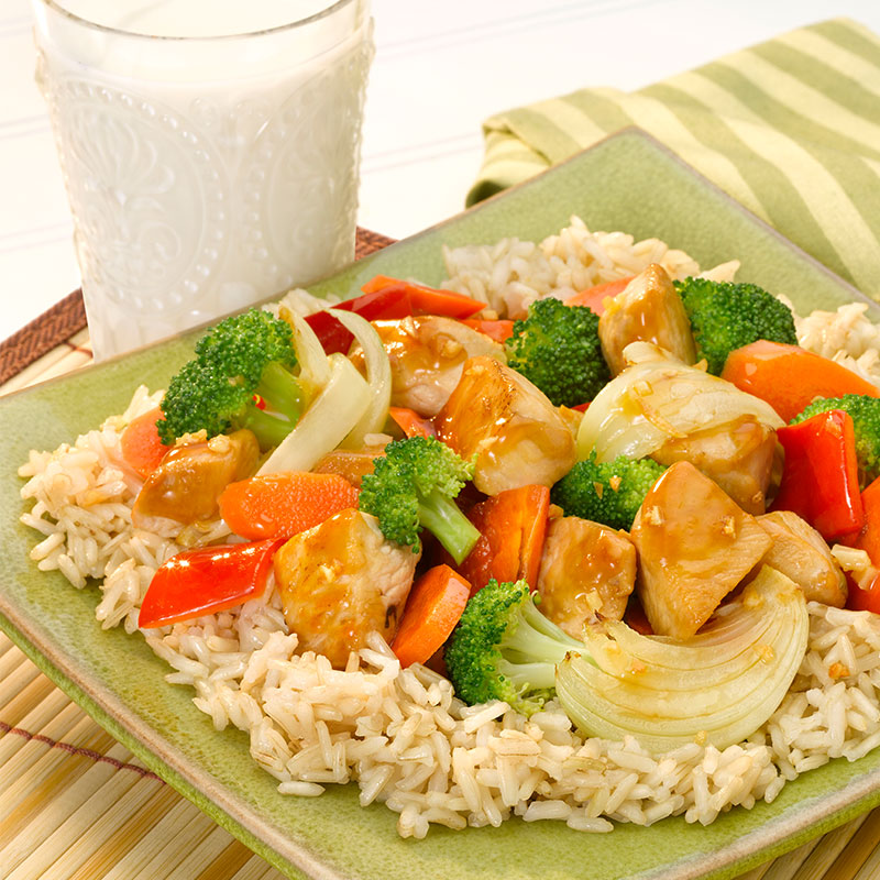 Side view of brown rice with chicken and vegetables on a green plate.