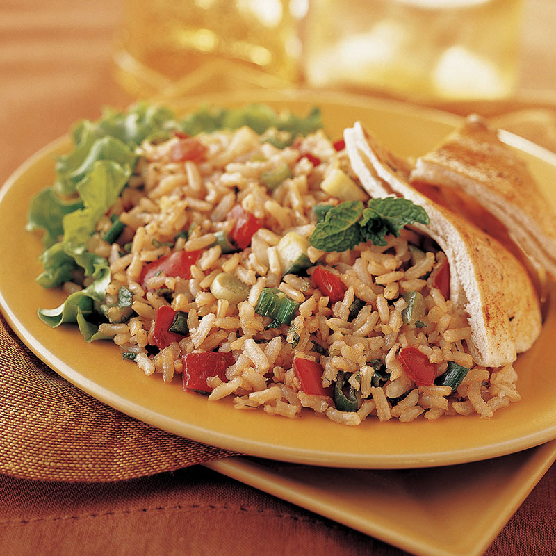 Side vide of brown rice tabbouleh on a yellow plate with lettuce and pita bread.