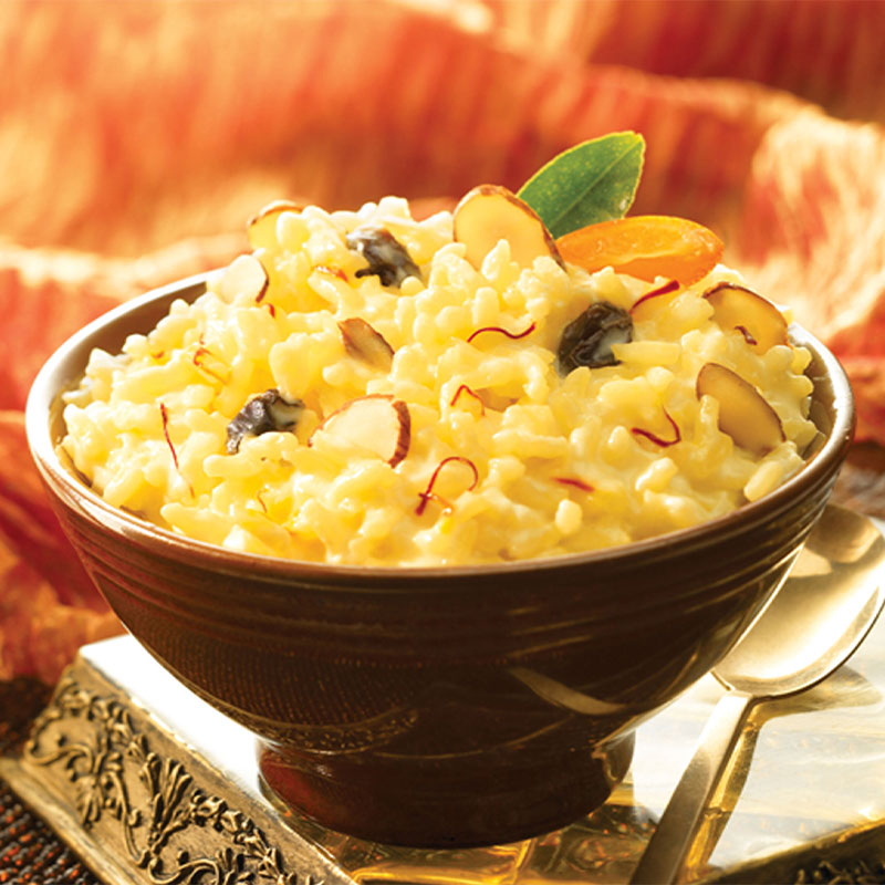 Side view of yellow Cardamom Saffron Rice Pudding in a bowl with a gold spoon to the side.