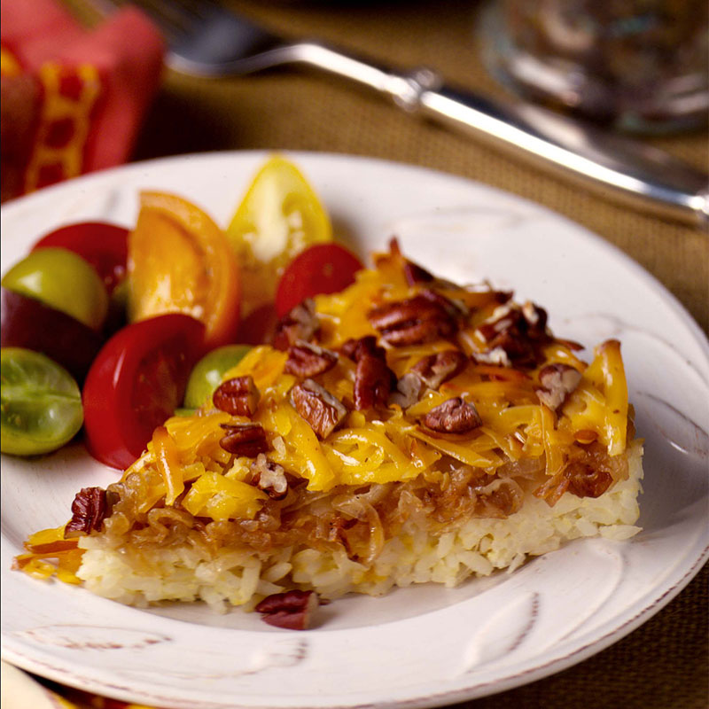A slice of Caramelized Onion, Smoked Gouda and Pecan Rice Tart on a white plate next to assorted vegetables.