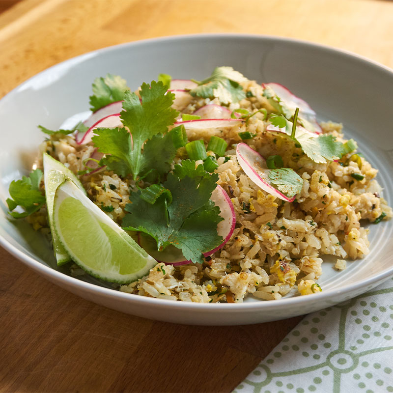 Overhead shot of crab fried rice in a white dish with lime wedges, garnish, and a radish slices.