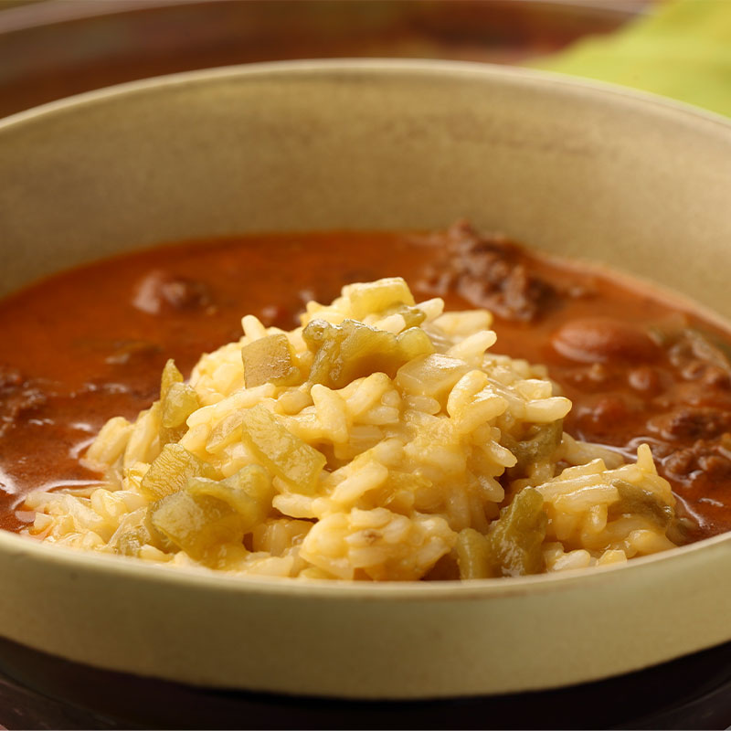 Zoomed in image of a bowl of chili topped with cheesy rice and peppers.