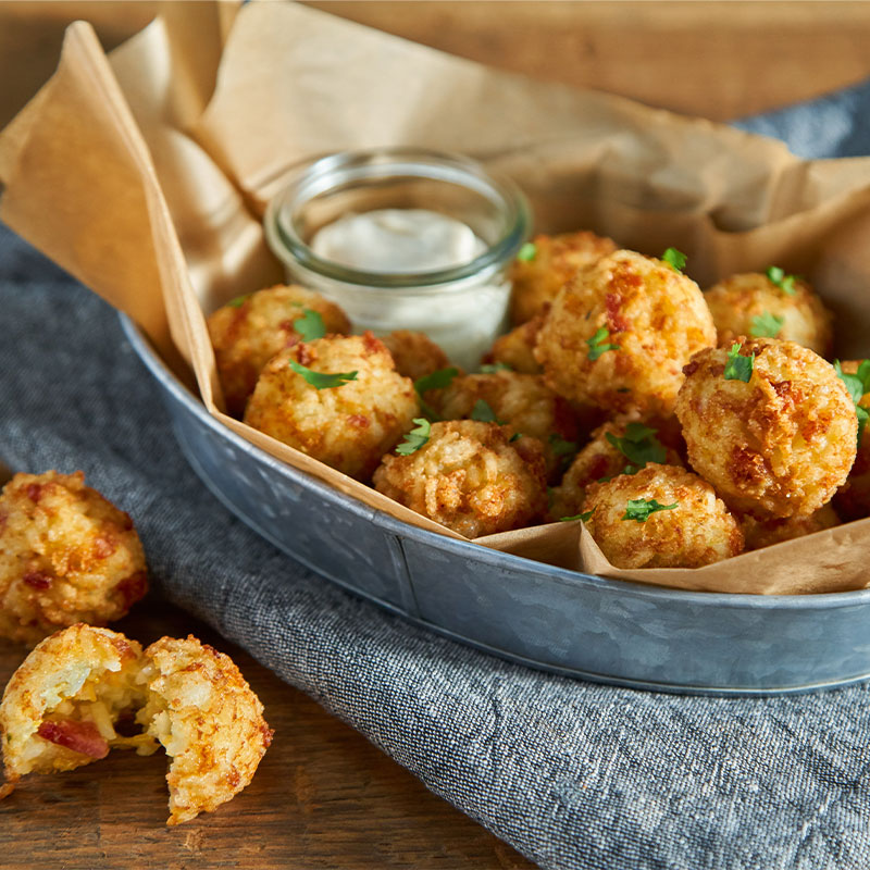 A platter of Cheesy Bacon Rice Tots plated with dipping sauce.