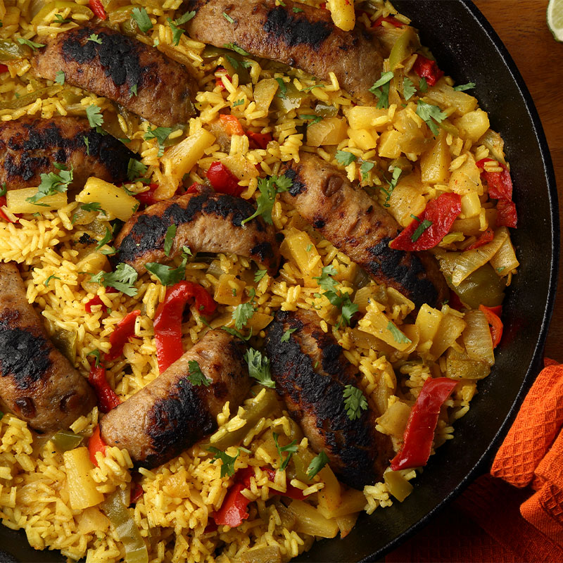 A skillet full of chicken-apple sausage and yellow rice with pineapple chunks and peppers.