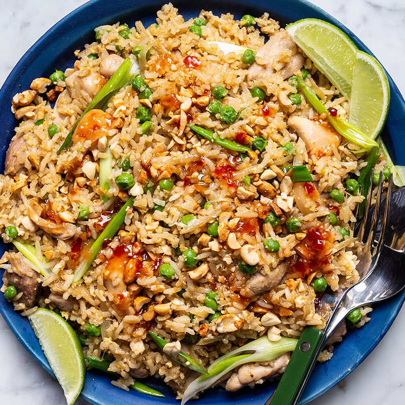 Overhead view of chicken green onion fried rice on a blue plate with lime wedges.