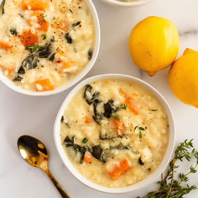 Overhead image of two bowls of Chicken Lemon Rice Soup on a table with lemons to the side.