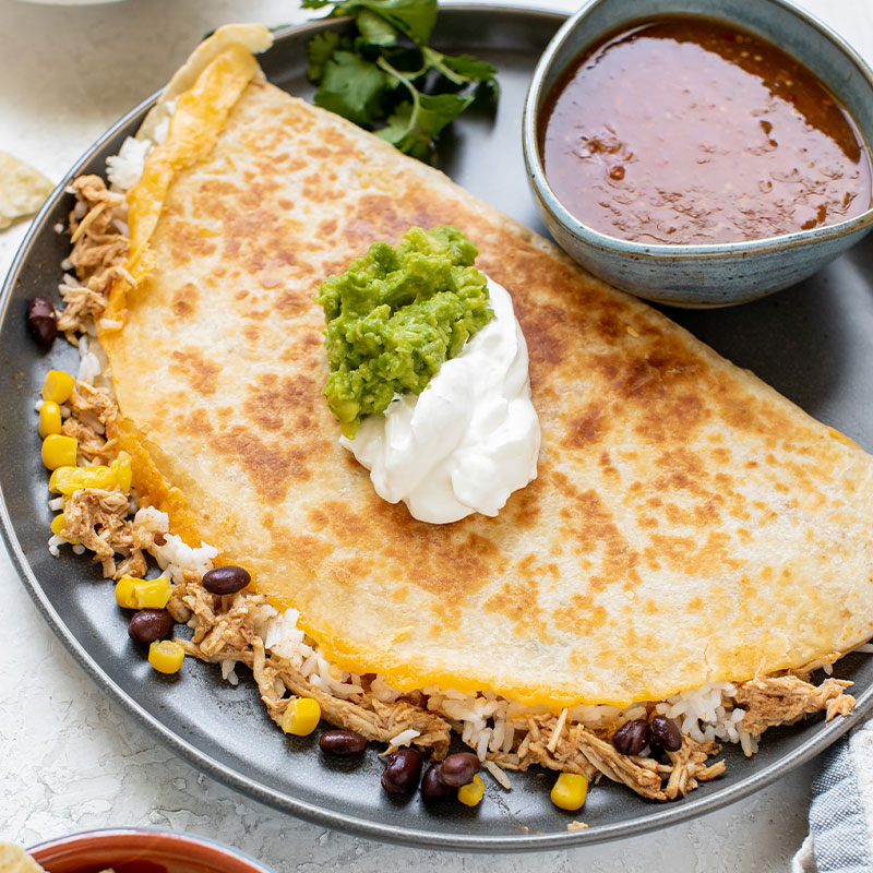 Chipotle Chicken & Rice Quesadilla A large Chipotle Chicken & Rice Quesadilla topped with guacamole and sour cream on a plate.