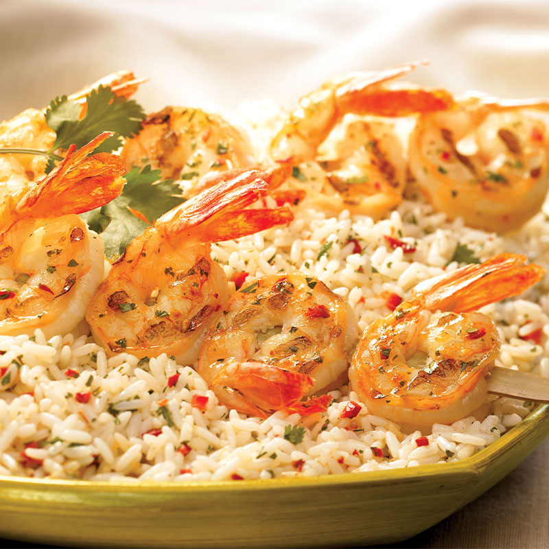 Two Cilantro Chimichurri Shrimp Skewers on top of a serving of rice.