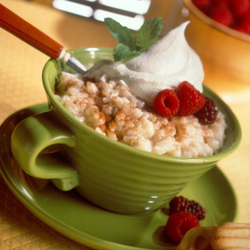 Side view of cinnamon rice pudding in a green mug topped with whipped cream and berries.