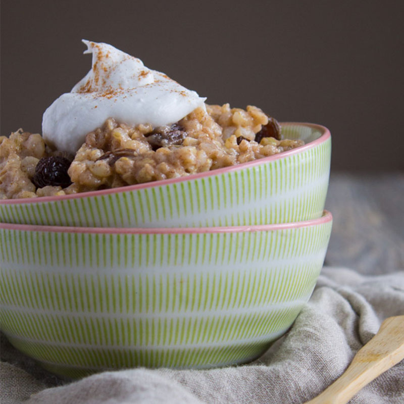 Close up view of coconut brown rice pudding topped with whipped cream in a green bowl.