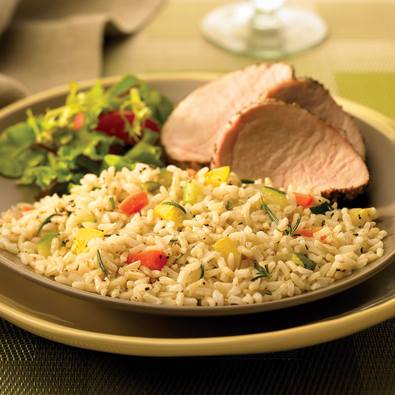 Side view of confetti rice pilaf on a plate with sliced ham and salad greens.