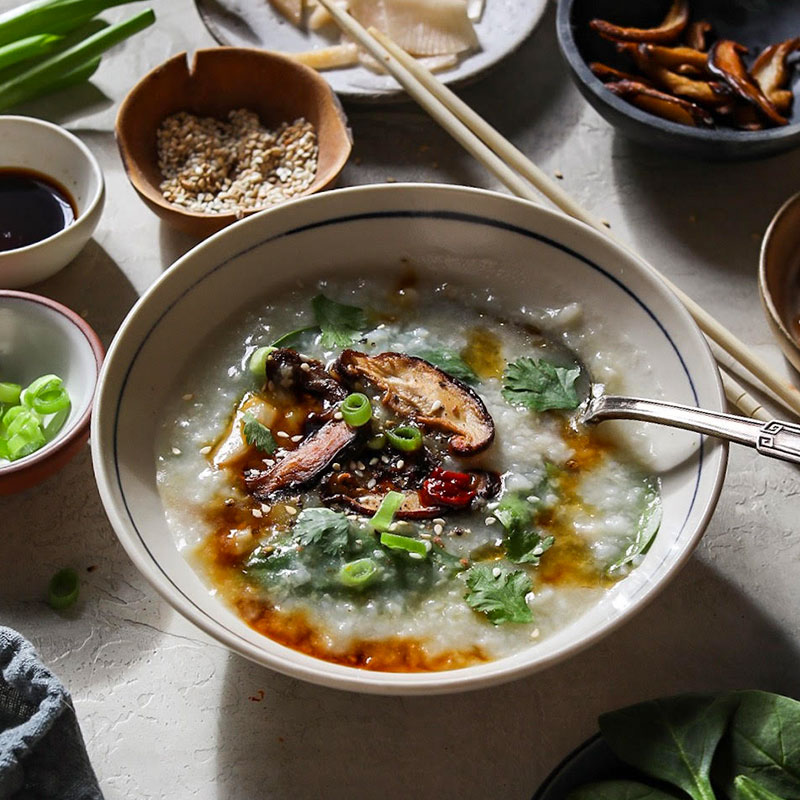 Overhead view of congee with spinach and shiitake mushrooms in a white bowl.