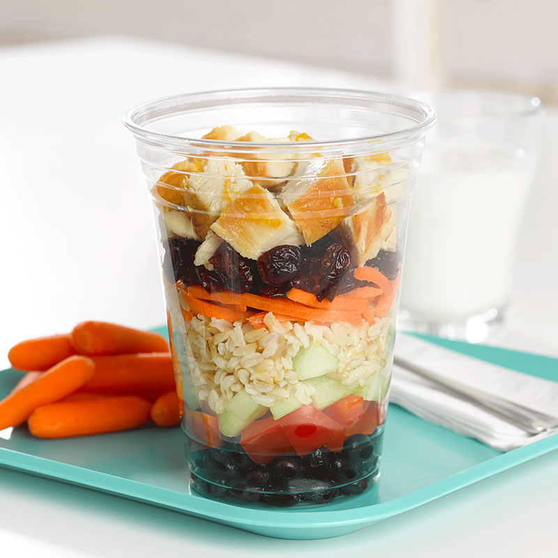 Side view of cranberry rice shaker salad in a clear cup on a school lunch tray.