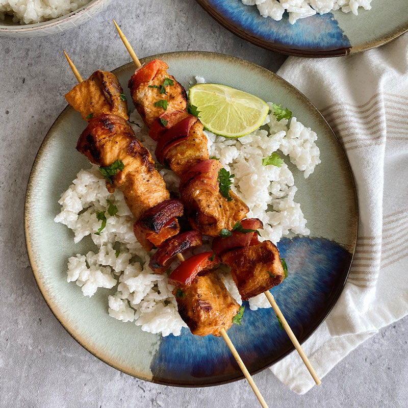 Overhead shot of two smoked salmon skewers on a bed of creamy coconut rice.