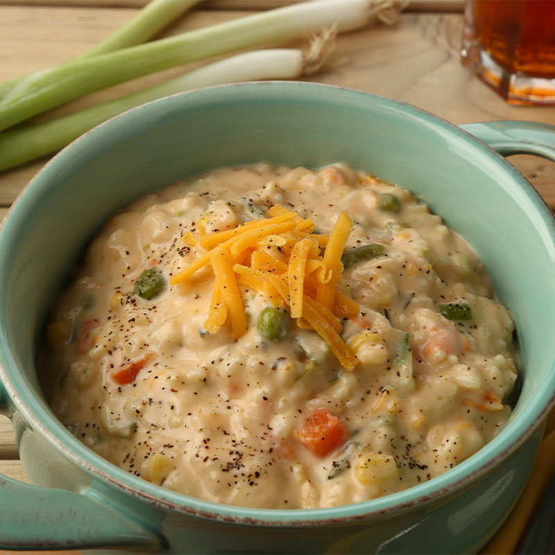 Overhead image of a large serving of creamy vegetable rice with peas, peppers, and corn exposed and topped with shredded 