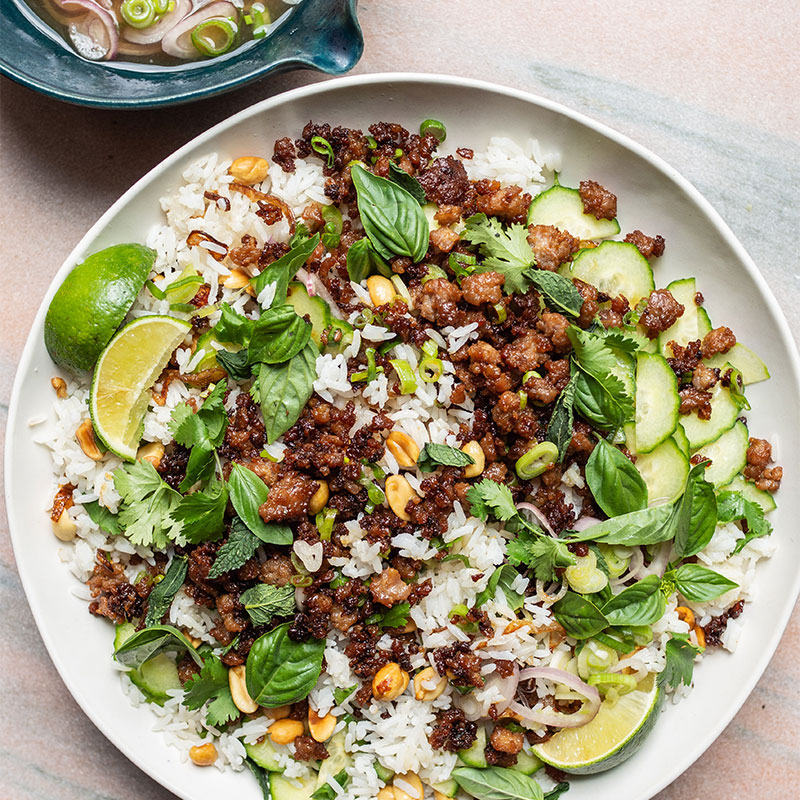 Overhead shot of Crispy Pork Rice Salad on a white dish garnished with cilantro and lime wedges.