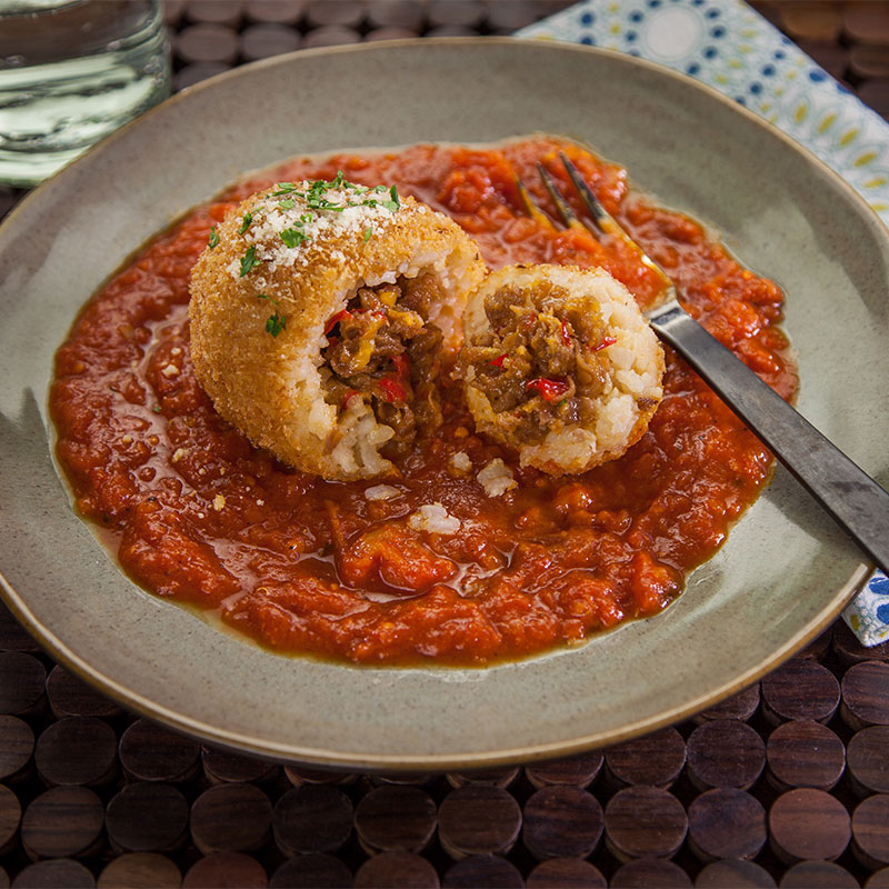 Crispy Rice Cherry Bomb Side view of one Crispy Rice Cherry Bomb cut in half atop marinara sauce.