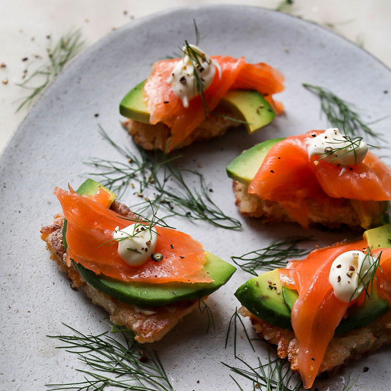 Four pieces of Crispy Sushi Rice with Smoked Salmon & Avocado on top.